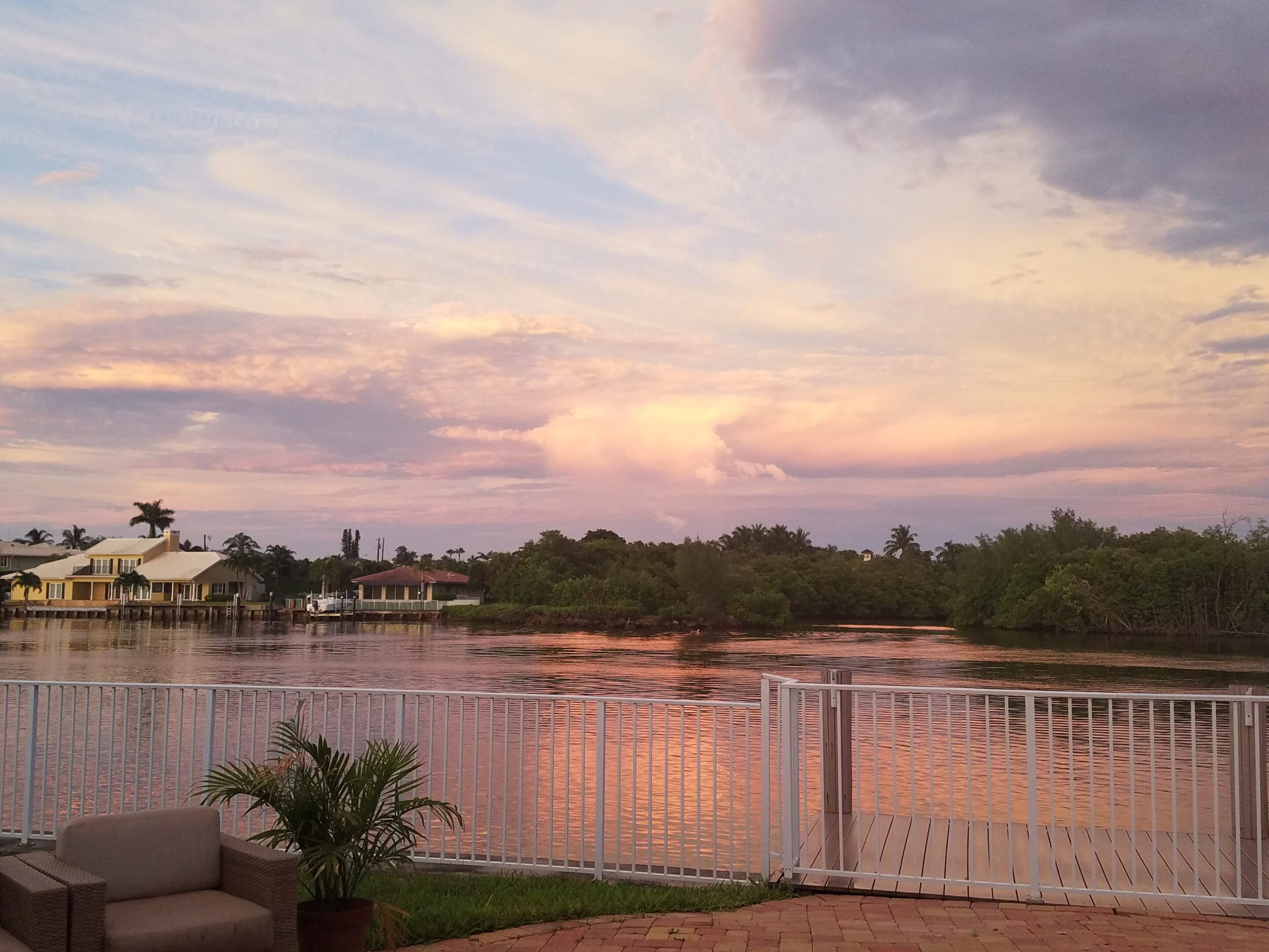Sunset reflecting over a calm river with houses and trees.