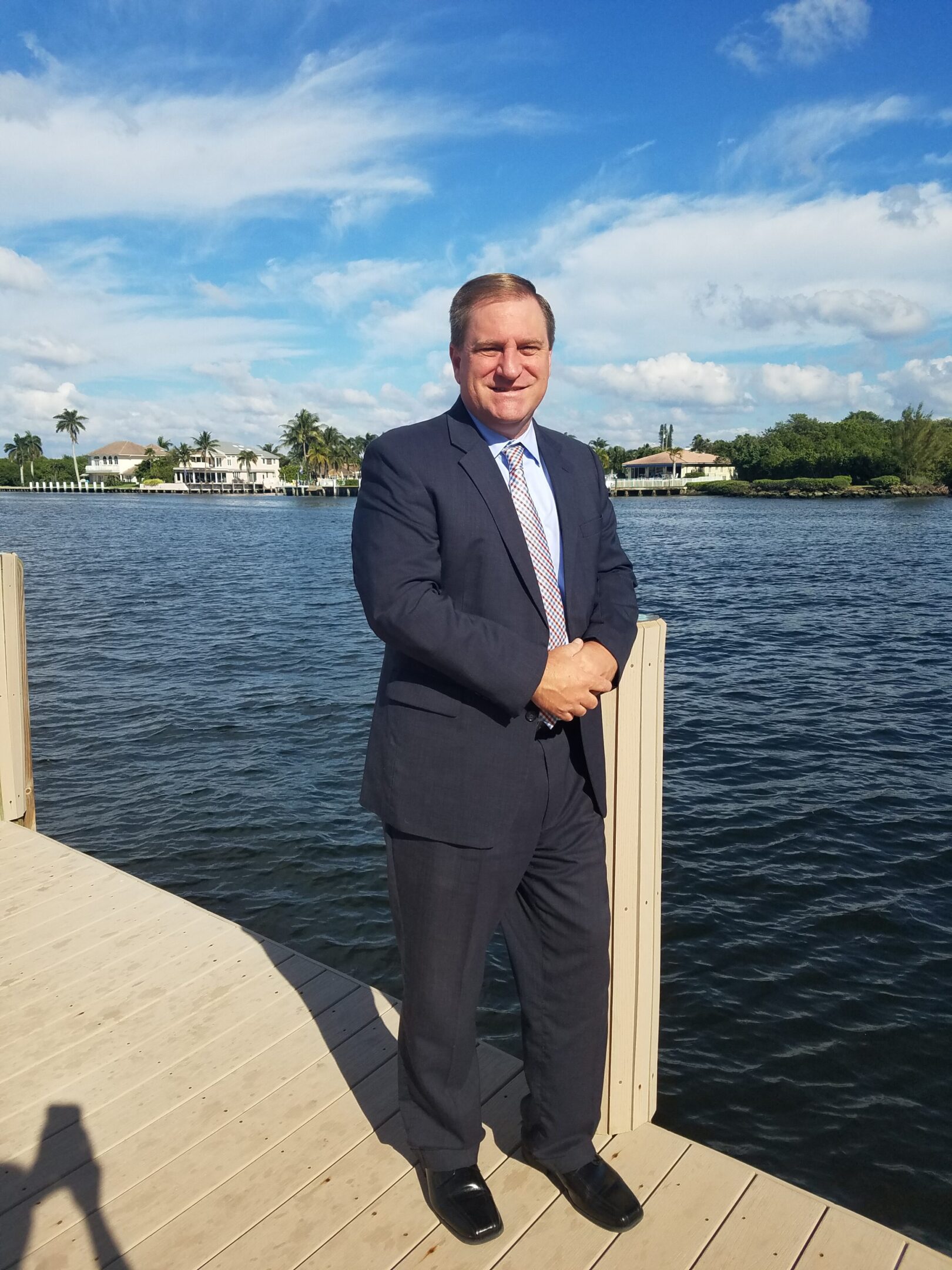 A man in a suit standing on a dock by the water.
