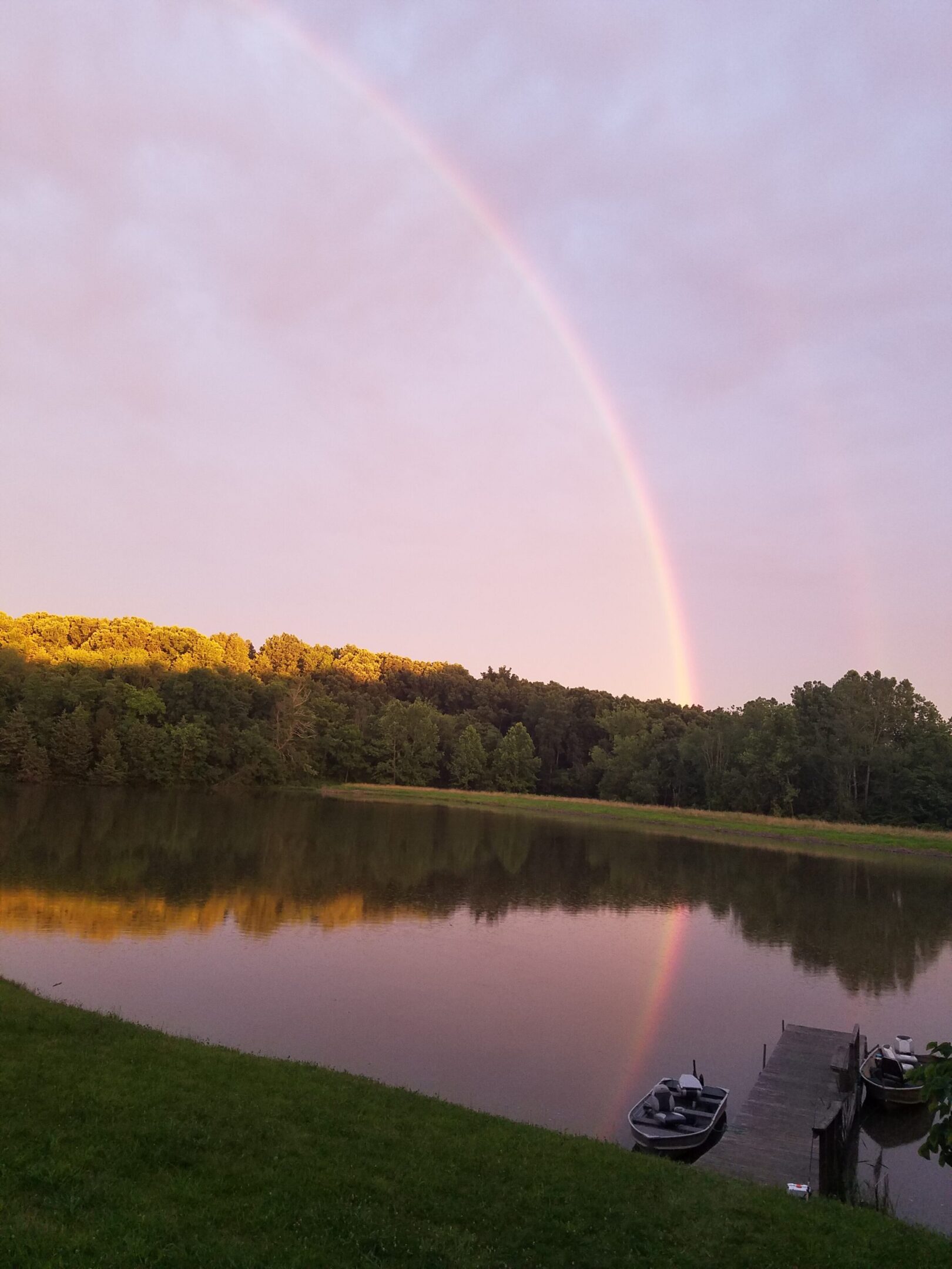 Rainbow arching over a lake with trees at sunset.